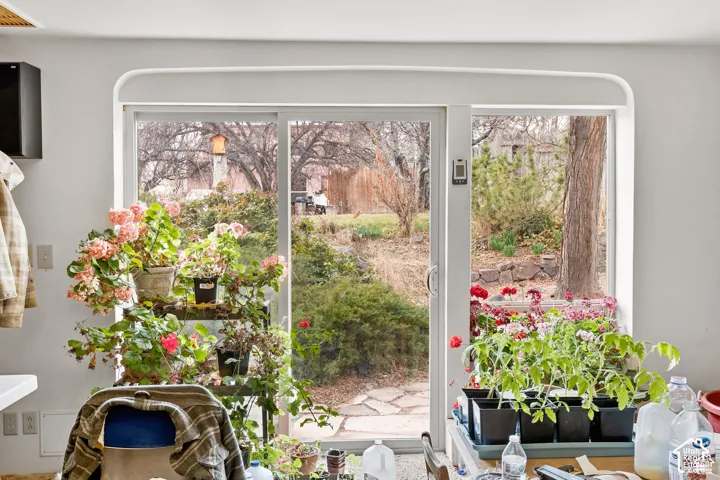 Sliding glass door leading to a stone patio with surrounding mature trees and landscaping