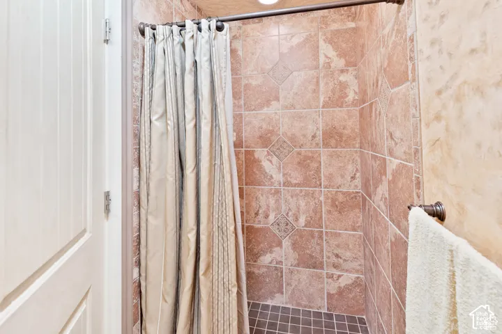 Shower enclosure featuring textured wall tiles, a contrasting mosaic tile floor, and an integrated ceiling light