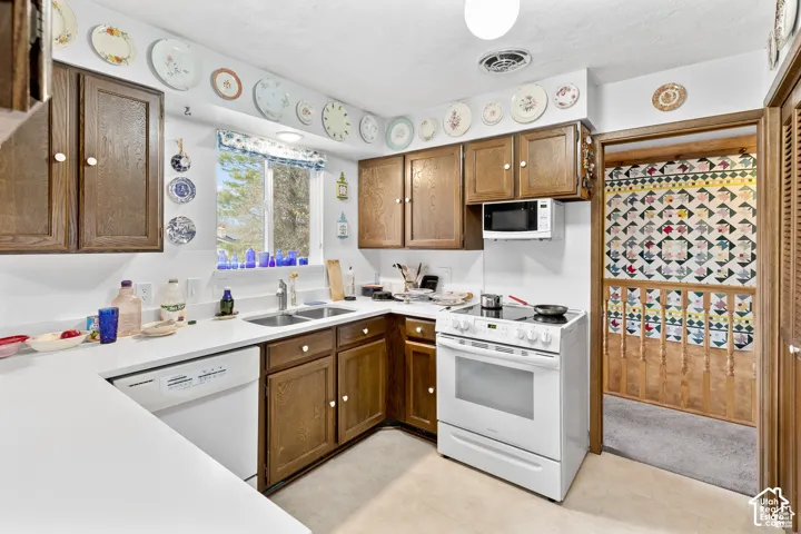 White countertops, wood-finish cabinetry, a white electric range, and a stainless steel double basin sink