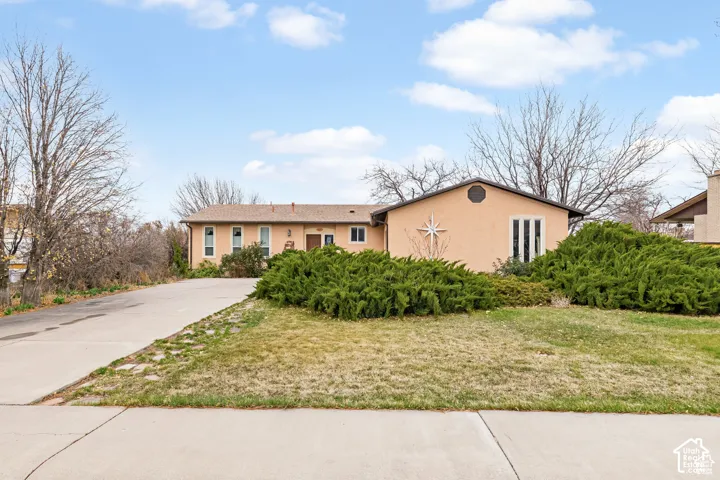 Stucco exterior residence with a concrete driveway, established shrubs, and a circular accent window