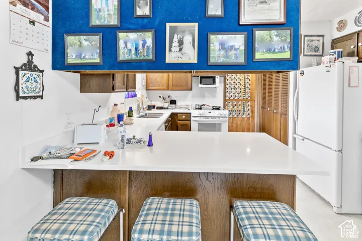 Kitchen featuring a breakfast bar with a white countertop, wood-finish cabinetry, and white appliances