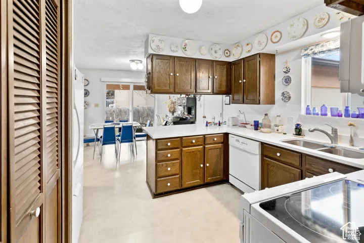 Laminate flooring, wood cabinetry with white knobs, white countertops, built-in dishwasher, and a double basin stainless steel sink