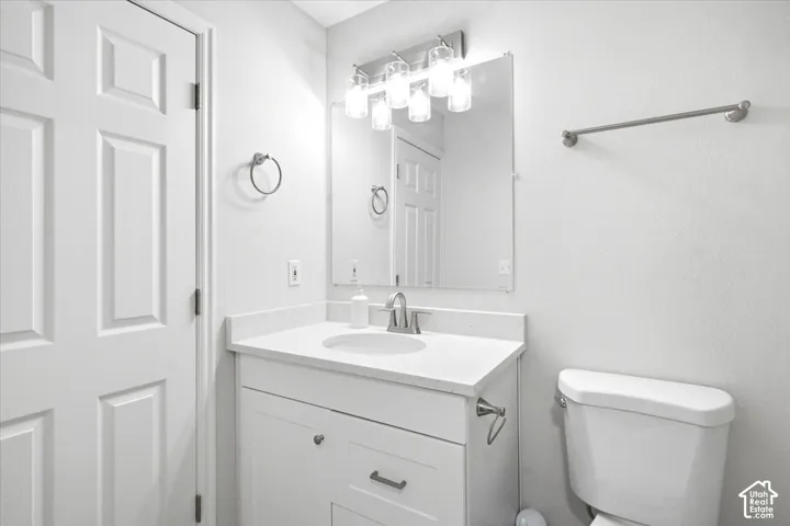 White paneled door, single vanity with a white quartz countertop and integrated sink, brushed nickel faucet, wall-mounted mirror, and overhead vanity lighting