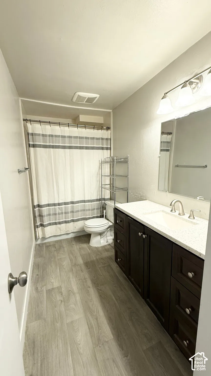 Wood-finish flooring, dark wood-tone vanity with a white countertop, chrome faucet, and integrated sink