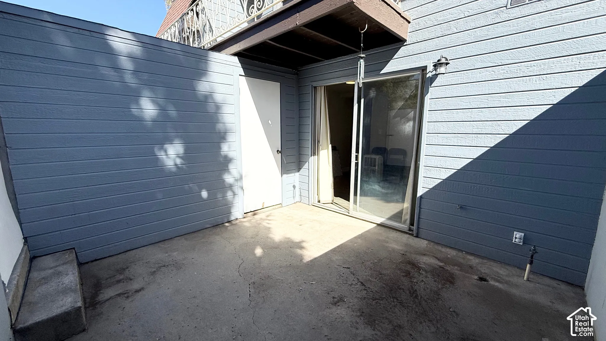 Private outdoor patio with a sliding glass door entry, exterior lighting fixture, and a solid privacy wall