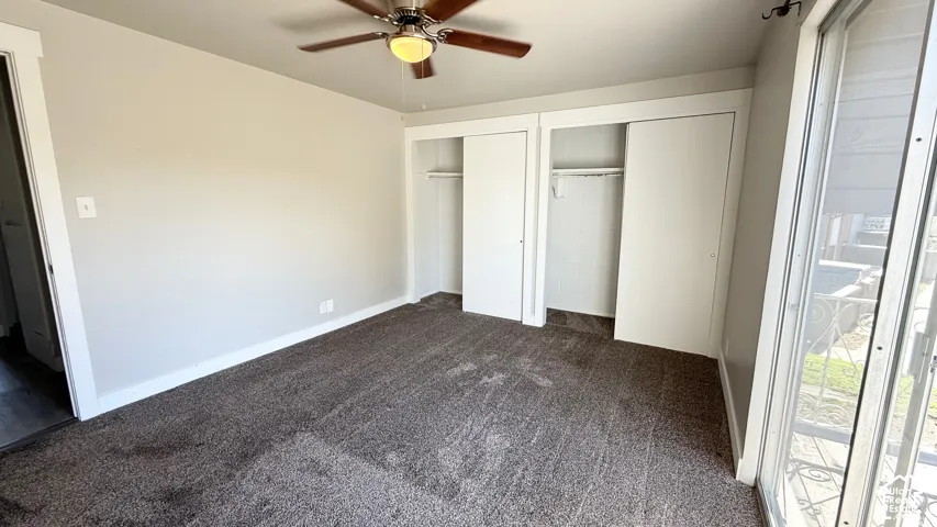 Light-colored walls, ceiling fan with light fixture, sliding closet doors, and dark carpet flooring