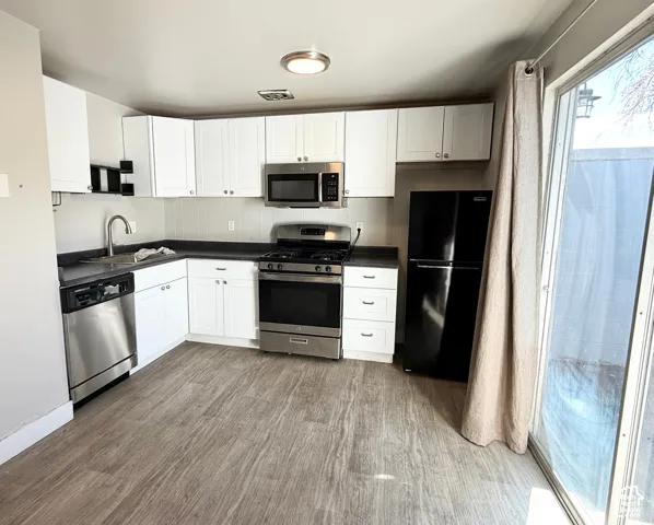 Wood-finish flooring, white shaker-style cabinetry, dark countertops, stainless steel appliances, and a sliding glass door