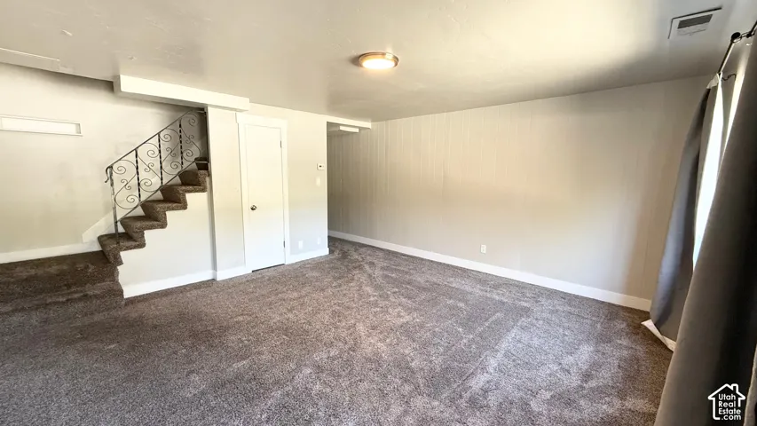 Spacious interior featuring patterned carpet flooring, a closed-stringer staircase with an ornate metal railing, and a flush-mount ceiling light fixture