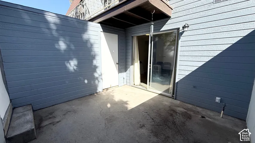Private outdoor patio with a sliding glass door entry, exterior lighting fixture, and a solid privacy wall