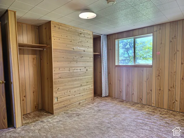 Room interior featuring wood-paneled walls, built-in closet storage with integrated shelving and rods, a sliding window, and a drop ceiling with a flush-mount light fixture