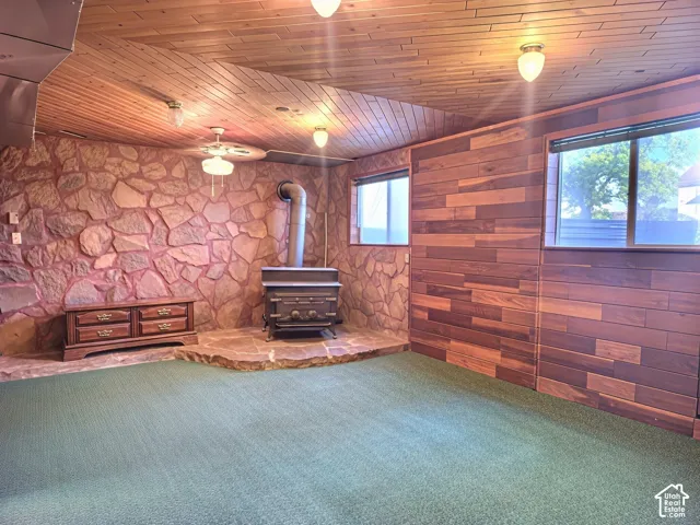 Interior featuring wood-plank ceiling, floor-to-ceiling stone accent wall, multi-tonal horizontal wood wall paneling, and a wood-burning stove on a raised stone hearth