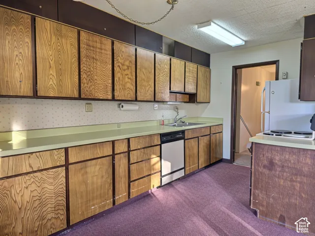 Kitchen featuring wood-finish cabinetry, solid-surface countertops, integrated stainless steel dishwasher, and overhead fluorescent lighting