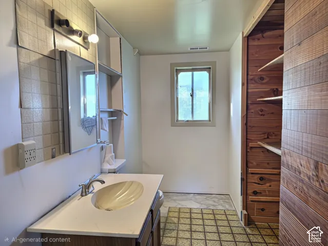 Bathroom featuring a vanity with a drop-in basin, wood-paneled walls, built-in shelving, a single-light vanity fixture, and tiled flooring