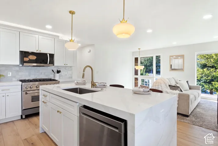 Modern kitchen featuring an expansive island with an undermount sink, brass-finish faucet, white shaker cabinetry, stainless steel appliances, and wood-finish flooring