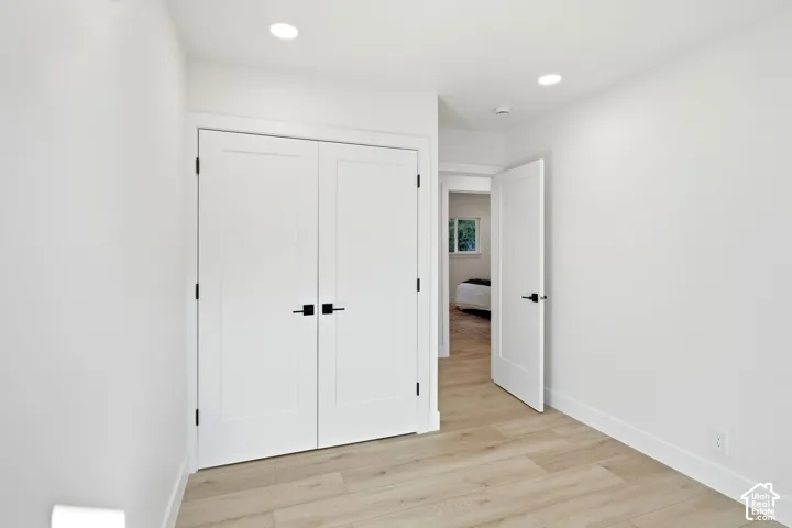 Recessed lighting, light wood-finish flooring, white walls, white doors with matte black hardware, and white trim