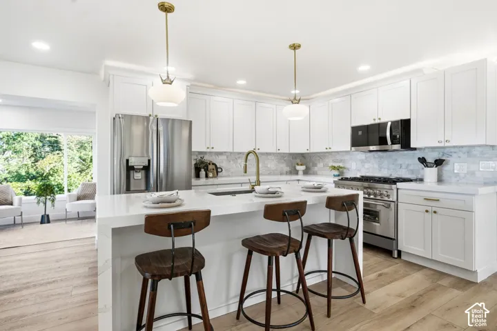 White shaker cabinetry, stainless steel appliances, quartz countertops, tile backsplash, and wood-finish flooring