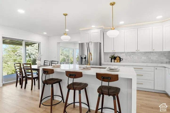 Modern kitchen featuring white cabinetry, a large center island with seating, a stainless steel refrigerator, and wood-finish flooring