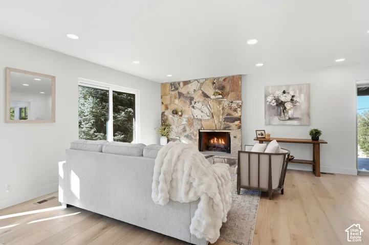 Spacious living area featuring wood-finish flooring, a stone-clad fireplace with hearth, recessed lighting, and a large sliding glass door