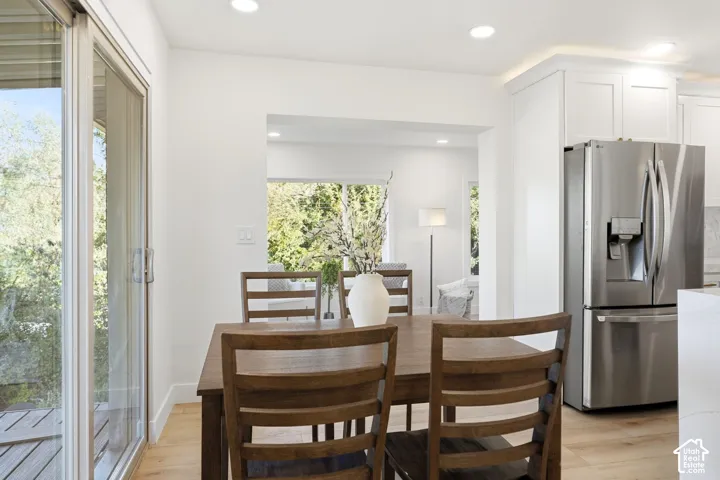 Sliding glass door to outdoor decking, recessed ceiling lighting, light wood-finish flooring, white cabinetry, and a stainless steel French door refrigerator