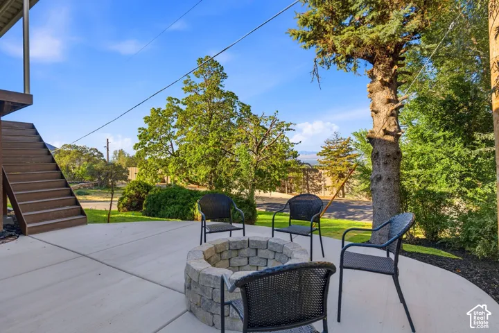 Concrete patio with a stone fire pit, surrounded by mature trees and landscaping