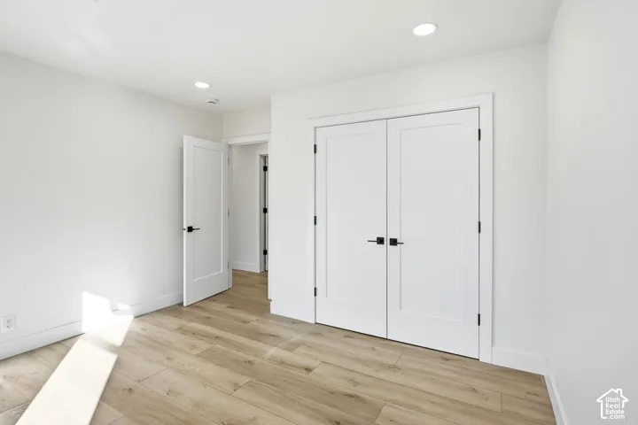 Bright bedroom featuring gleaming wood-finish flooring, recessed ceiling lighting, and dual white panel closet doors with black hardware