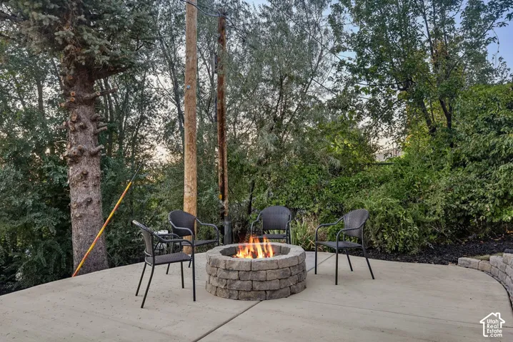 Concrete patio with a stone-finish fire pit, surrounded by lush mature trees and a retaining wall