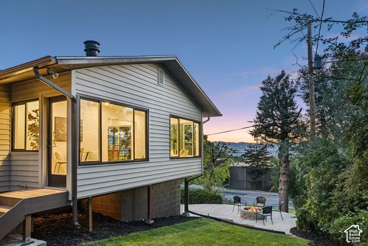 Exterior with horizontal siding, multiple large windows with dark frames, and a lower-level patio featuring a built-in fire pit
