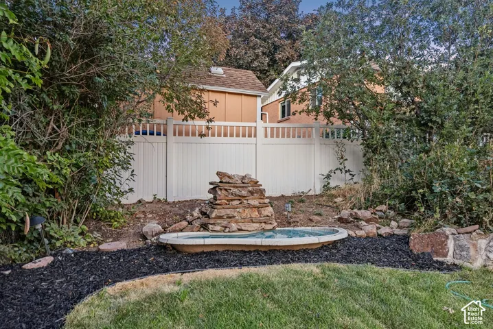 Outdoor water feature with a stacked stone design, surrounded by dark ground cover and green lawn