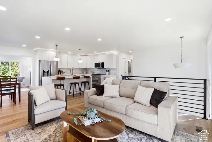 Open-concept living area with light wood-finish flooring, a contemporary horizontal bar railing, recessed lighting, and a modern chandelier