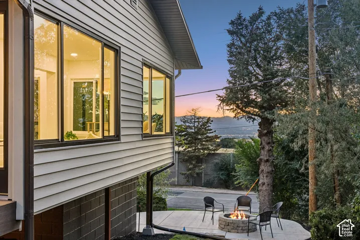 Siding exterior with multiple windows, concrete block foundation, integrated rain gutters, and an exterior patio with a built-in stone fire pit