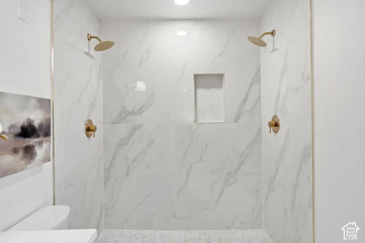 Walk-in shower with large format tile walls, dual gold-finish shower heads, gold-finish fixtures, and a recessed shower niche