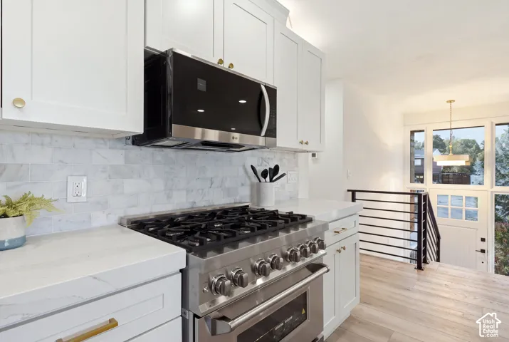 Kitchen featuring stainless steel range with overhead microwave, white shaker-style cabinetry, light-toned countertops, and a tiled backsplash