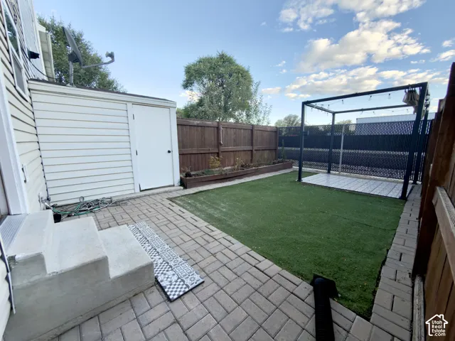 Patio area with paver stones, artificial turf, wood fence, shed, and a freestanding pergola with string lighting