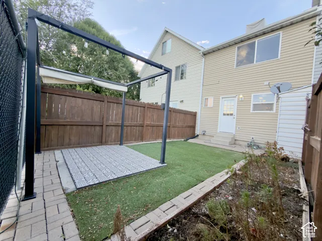 Patio area with paver stones, artificial turf, wood fence, shed, and a freestanding pergola with string lighting