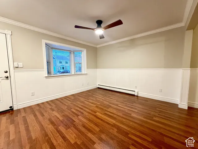 Laminate flooring, bay window, wainscoting, crown molding, and ceiling fan with integrated lighting
