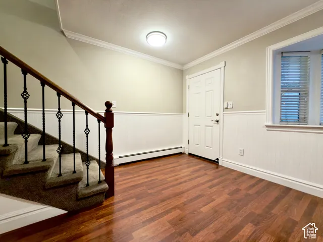 Front door area with laminate flooring, wainscoting, crown molding, and a carpeted staircase with decorative iron spindles