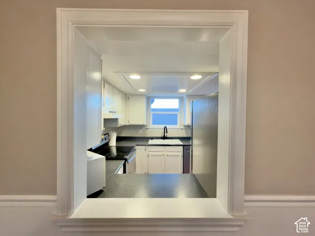 Kitchen pass-through with white trim, black countertops, white cabinetry, a stainless steel refrigerator, and recessed lighting