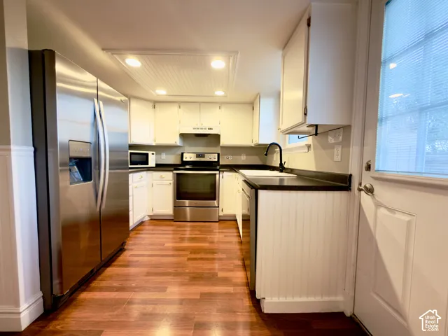 Kitchen featuring stainless steel appliances, white cabinetry, dark countertops, wood-finish flooring, and recessed lighting-all appliances included