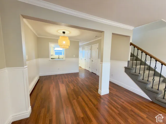 Dining area with laminate flooring, wainscoting, crown molding, open archway, and staircase with wrought iron balusters