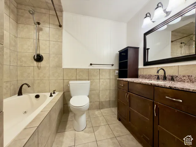 Tile flooring and bath surround, large corner jetted tub, dark wood vanity with a granite countertop, and a framed mirror with an overhead light fixture