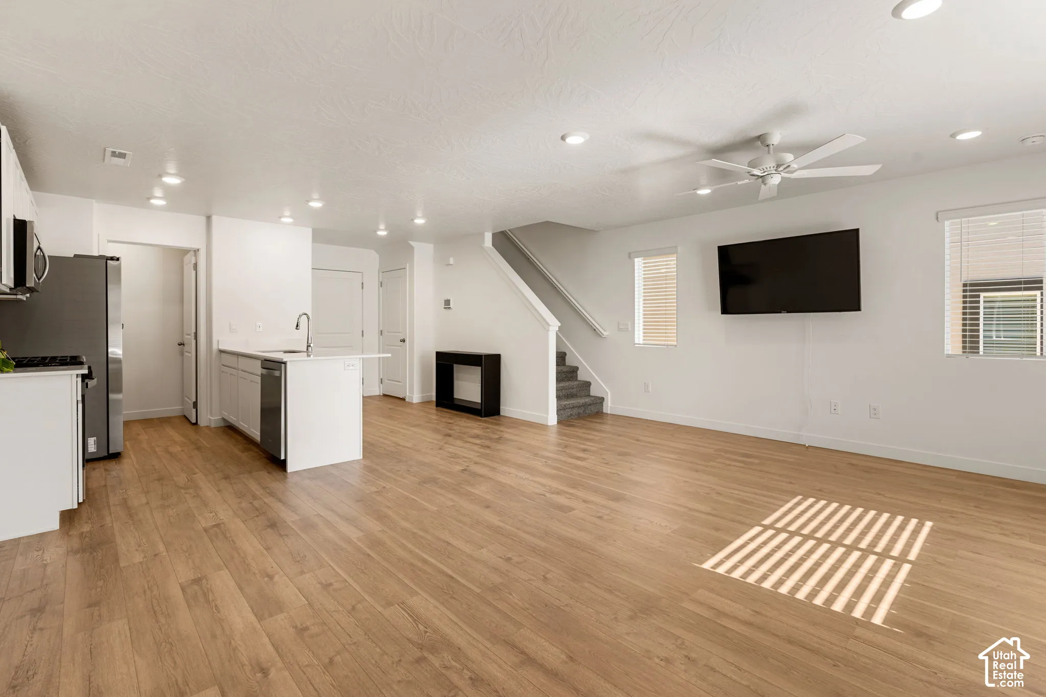 Open-concept living area featuring wood-finish flooring, recessed lighting, a ceiling fan, and a kitchen island with sink