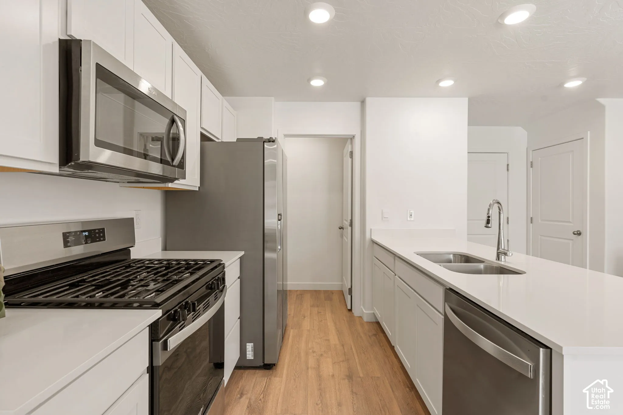 Modern kitchen featuring stainless steel appliances, white cabinetry, light wood-finish flooring, and recessed ceiling lighting