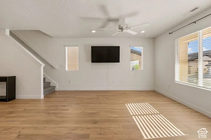 Spacious room featuring wood-finish flooring, multiple windows with blinds, a ceiling fan, and recessed lighting
