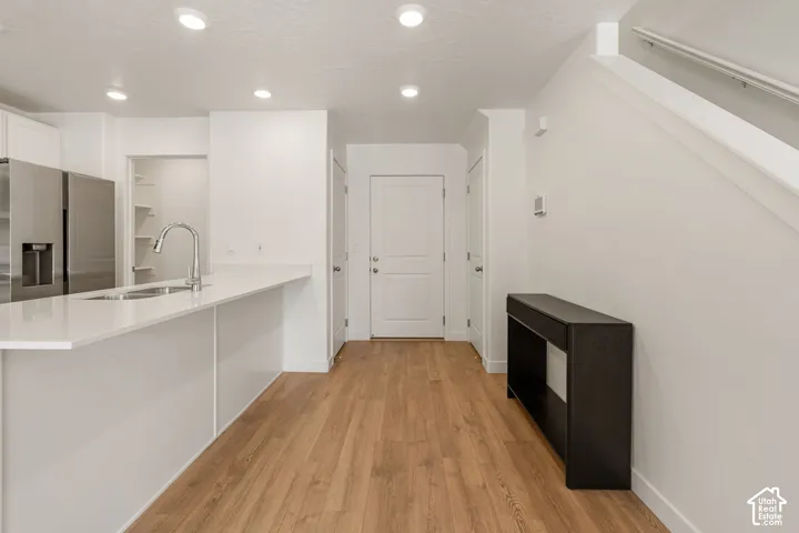 Open-concept design featuring wood-finish flooring, a kitchen island with a built-in sink and gooseneck faucet, stainless steel refrigerator, and recessed lighting