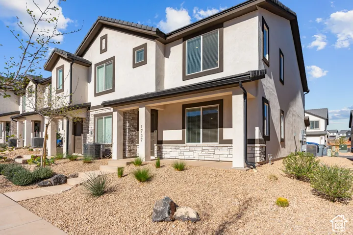 Two-story stucco exterior featuring stone accents, covered front porch, and dark-framed windows