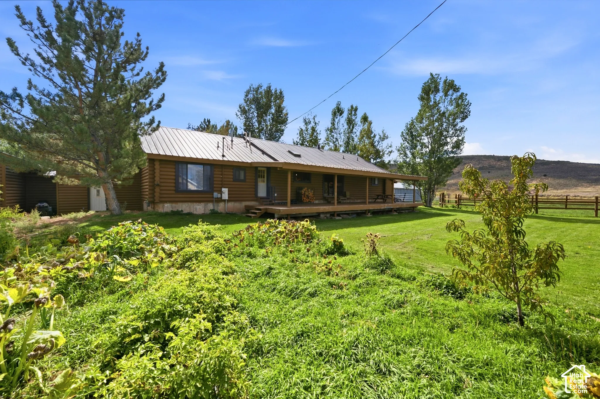 Log-sided residence with a metal roof, an expansive wooden porch, and an attached shed, set against a distant hillside
