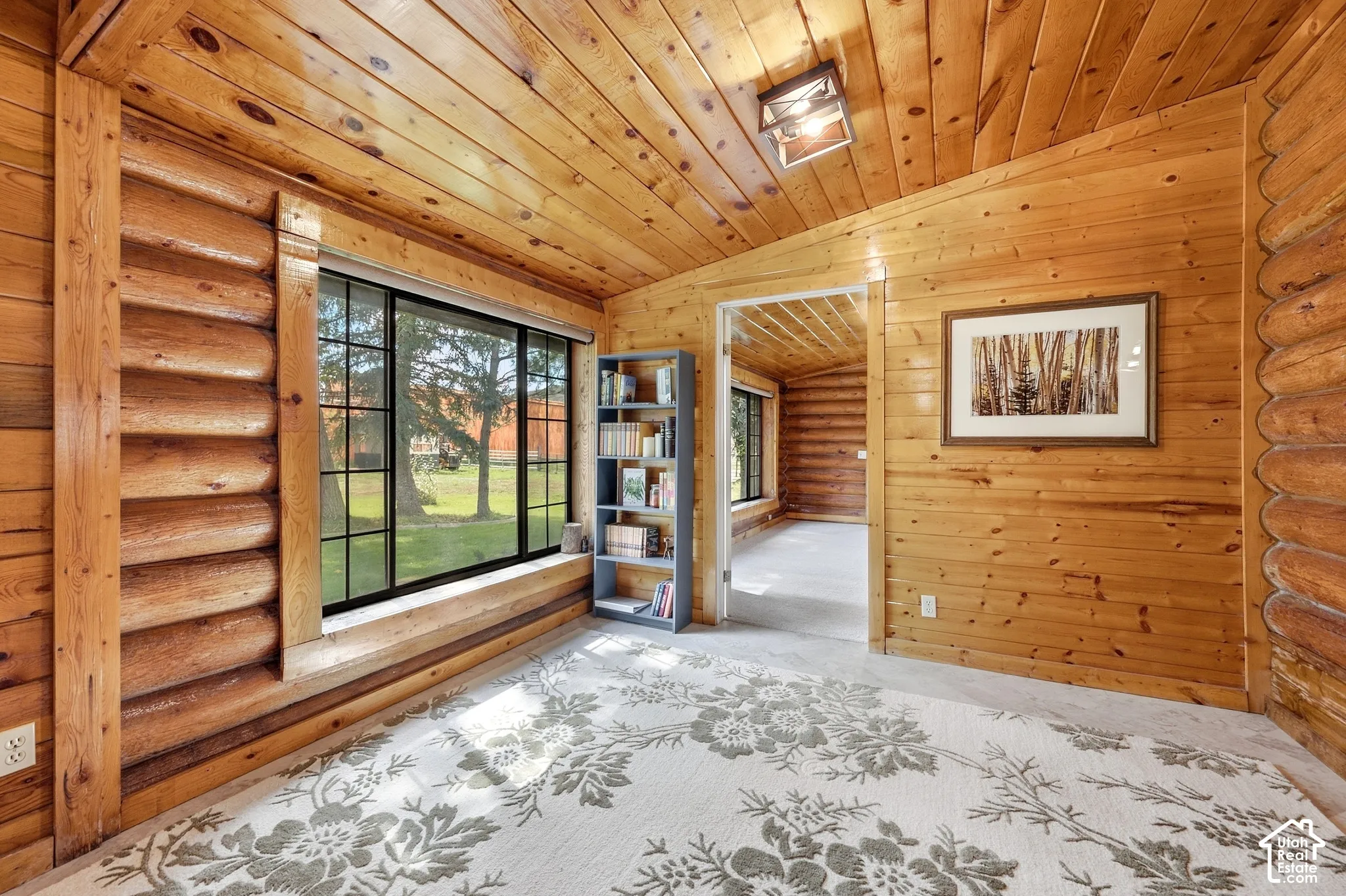Natural wood-paneled walls and ceiling, exposed log-style wall, and a large window with black framing