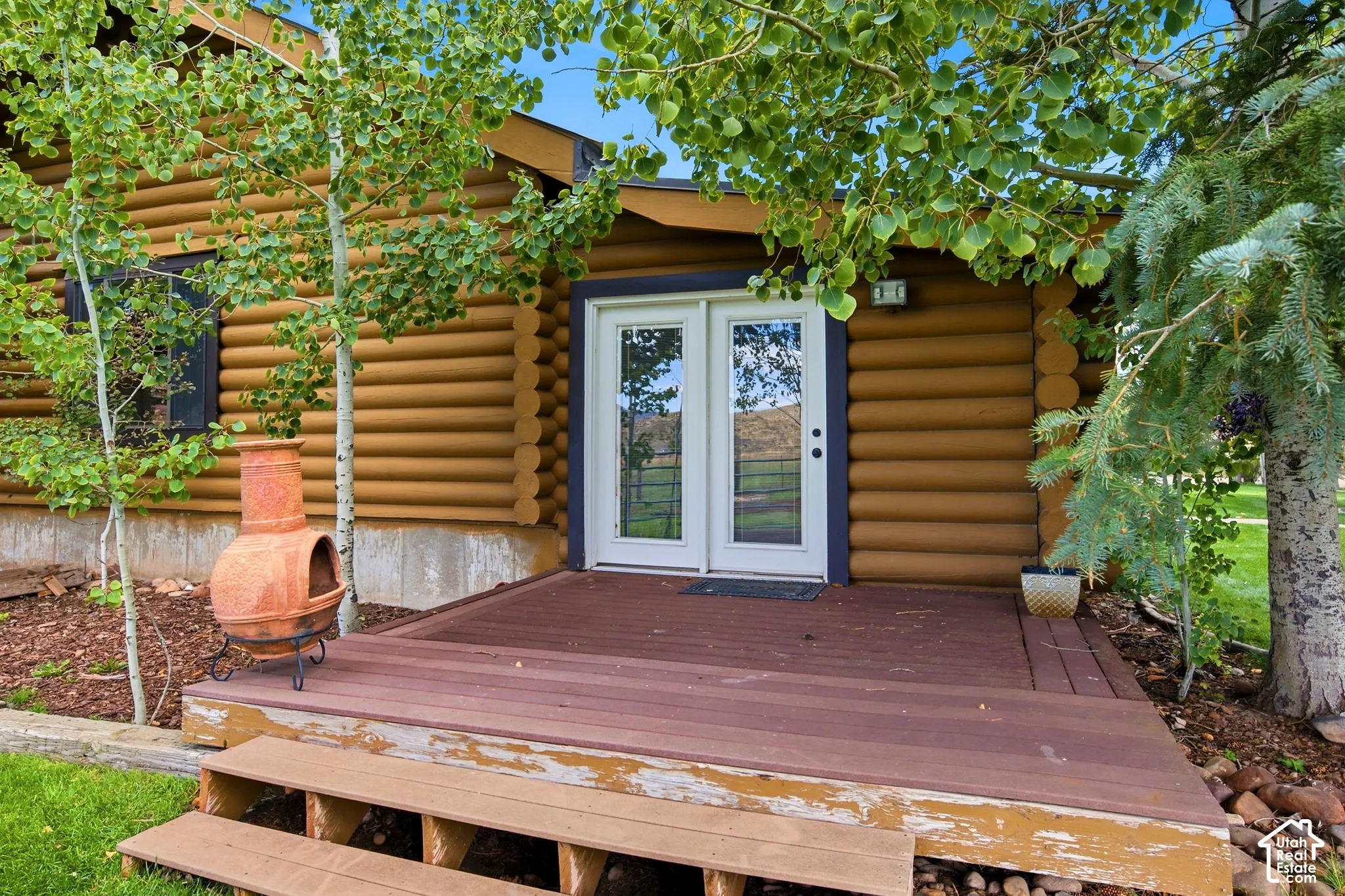 Log cabin exterior with a wood deck, white French patio doors, and natural landscaping