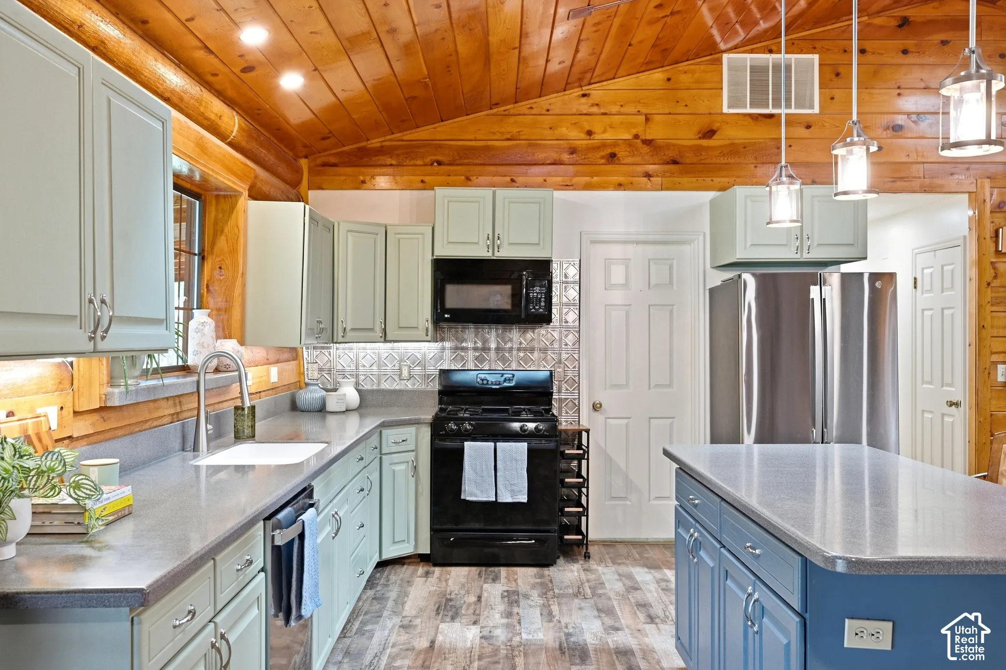 Kitchen featuring a vaulted wood-paneled ceiling, light-toned cabinetry, stainless steel refrigerator, black range, and an island with pendant lighting