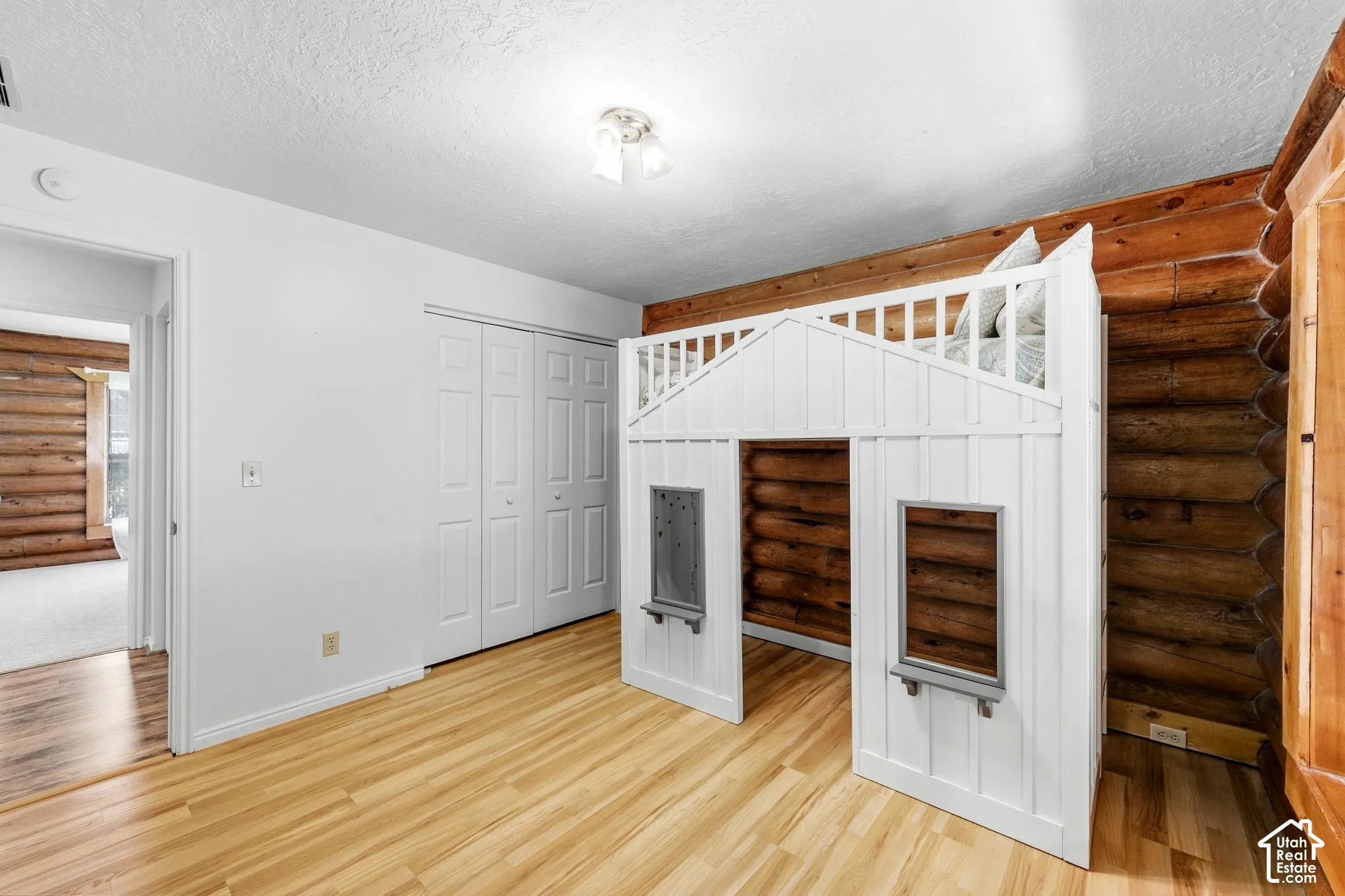 Wood-finish flooring with a white built-in bunk bed structure, white bi-fold closet doors, and exposed log wall construction
